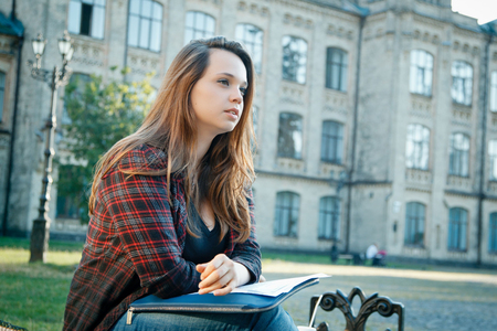 beautiful girl student sitting on bench near universityの写真素材