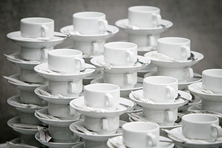 Piles of empty white ceramic cups with saucers, teaspoons and sachets of sugar on a gray backgroundの写真素材