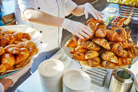 Hands in white gloves of two caters, one of which spreads croissants on a dish, and the other holds a dish with croissantsの写真素材