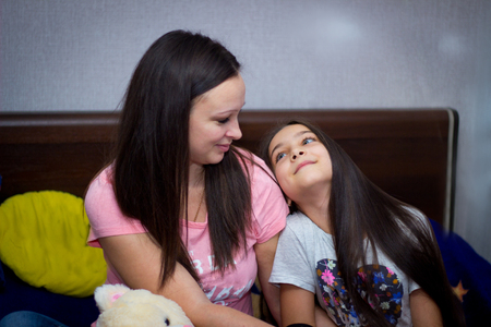 beautiful mom and little daughter chatting sitting on the sofaの写真素材
