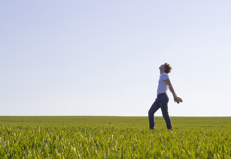 boy teenager walking on a field covered with green shoots of wheatの写真素材