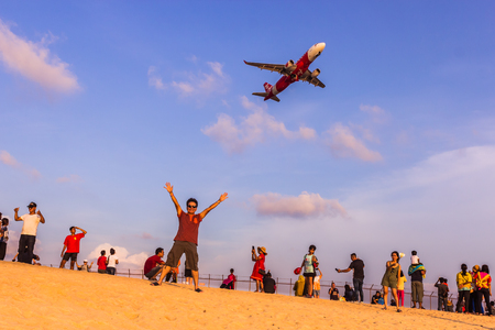 Phuket, Thailand - April 14, 2019: Tourists enjoy taking a picture with the airplane flying over them as the background, at the Mai Khao Beach, the edge of Phuket International Airport,Thailandのeditorial素材