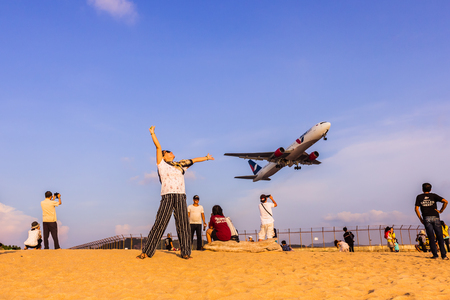 Phuket, Thailand - April 14, 2019: Tourists enjoy taking a picture with the airplane flying over them as the background, at the Mai Khao Beach, the edge of Phuket International Airport,Thailandのeditorial素材