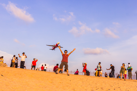 Phuket, Thailand - April 14, 2019: Tourists enjoy taking a picture with the airplane flying over them as the background, at the Mai Khao Beach, the edge of Phuket International Airport,Thailandのeditorial素材