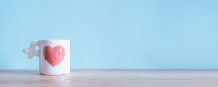 White Ceramic Coffee Cup with pink heart on the wooden tables and light blue walls. For you valentines background.の写真素材