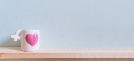 White Ceramic Coffee Cup with pink heart on the wooden tables and light blue walls. For you valentines background.の写真素材