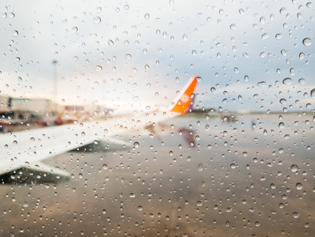 Abstract defocused blur of airplane at airport with sunset after the heavy rain. -Focus on raindrops windows glass.の写真素材