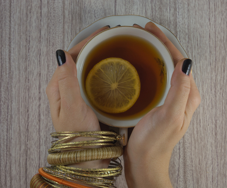 cup of tea with lemon in a female hand with braceletsの写真素材
