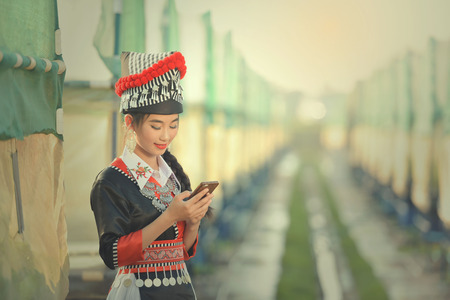 Tribal Asian woman wearing traditional dress texting smartphone.のeditorial素材