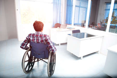 A side view of a Thai-Asian man working from work using a wheelchair, simple gray interior with copy space.の写真素材