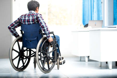 A side view of a Thai-Asian man working from work using a wheelchair, simple gray interior with copy space.の写真素材