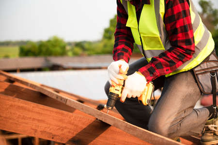 Builders in work clothes install new roofing tools, roofing tools, electric drill and use them on new wooden roofs with metal sheetsの写真素材