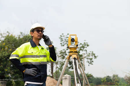 A young surveying engineer is measuring the level at a construction site. Surveyors certify accurate measurements before proceeding with the dormitory construction project.の写真素材