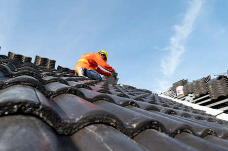 Builders in work clothes install new roofing tools, roofing tools, electric drill and use them on new wooden roofs with metal sheetsの写真素材