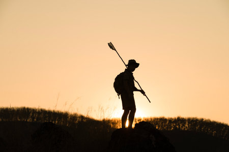 Silhouette of America Boy Scouts holding flag on top of mountain with blue sky and sunlight. It...