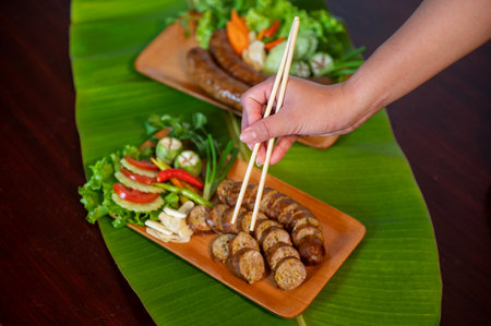 A Thai restaurant cook tastes delicious grilled herbed pork sausages from the barbeque served in the restaurant. Close-up shot of Thai sausage with fresh vegetable side dish, Thai foodの写真素材