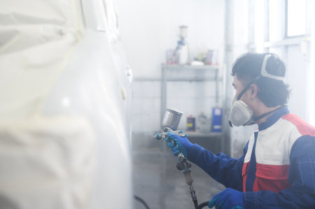 Asian auto mechanic wearing protective suit and respirator paints car body bumpers in paint room,spraying cars in paint roomの写真素材