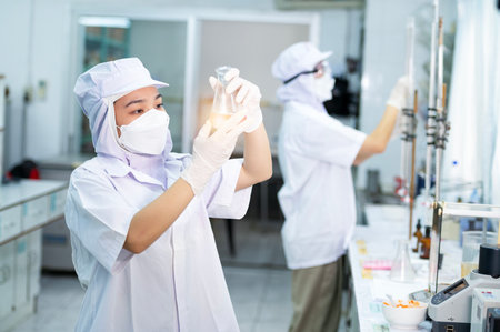 Asian female specialist in quality control lab examining tomato ingredient food in research lab, food industryの写真素材