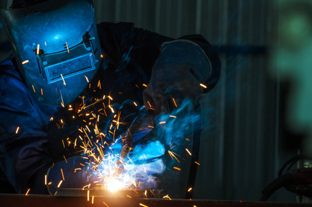 Industrial workers at steel structure welding plant A welder is welding metal parts in a small workshop.の写真素材