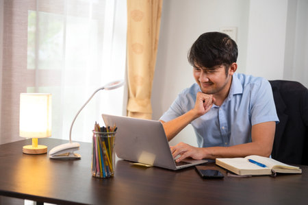 Asian young businessman smiling typing on laptop Happy businessman working on strategy at home office desk home office planの写真素材