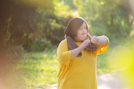 Girl with Down syndrome or autism looking at the time While walking outdoors in the parkの写真素材