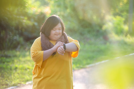 Girl with Down syndrome or autism looking at the time While walking outdoors in the parkの写真素材