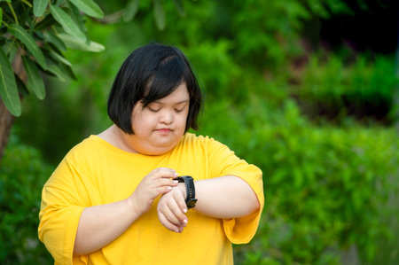 Girl with Down syndrome or autism looking at the time While walking outdoors in the parkの写真素材