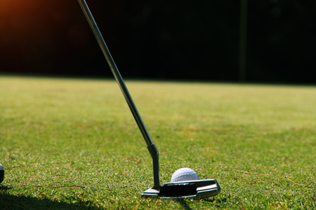 Golfer putting golf ball on the green golf. lens flare on sun set evening time.の写真素材