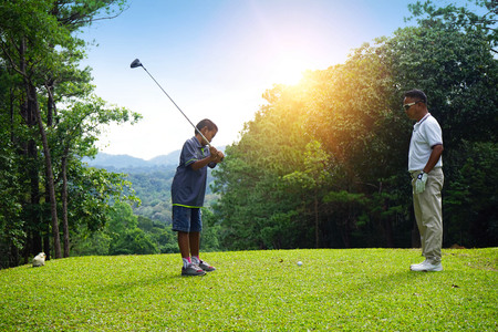 Man teaching Asian young to play golf while standing on field. Personal trainer giving lesson on golf course.の写真素材