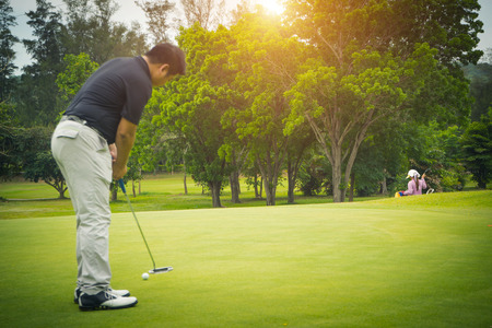 Golfer putting golf in the evening golf course, on sun set evening time. Man playing golf on a golf course in the sun.の写真素材