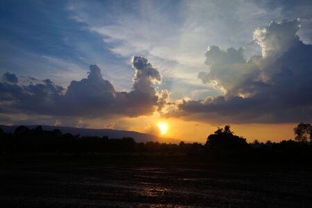 Colorful dramatic sunset sky with the sun of orange tones behind the mountains in the evening time.                                の写真素材