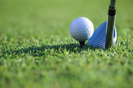 Golf clubs and golf balls on a green lawn in a beautiful golf course with morning sunshine.Close up of golf ball on a tee with the golf clubs ready to hit the ball.の写真素材