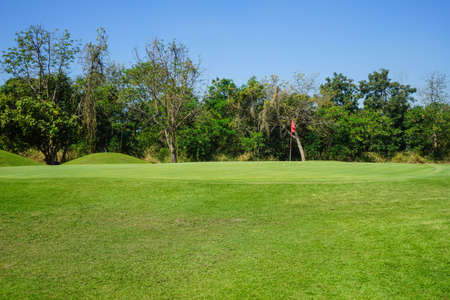 Red flag at the beautiful golf course at the sunrise time. Beautiful golf course in a sunny day. Background evening golf course has sunlight shining down. Golf course in the countrysideの写真素材