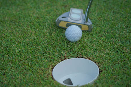 Golf clubs and golf balls on a green lawn in a beautiful golf course with morning sunshine. The ball at the hole on the golf course.の写真素材