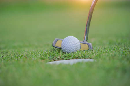 Golf clubs and golf balls on a green lawn in a beautiful golf course with morning sunshine. The ball at the hole on the golf course.の写真素材