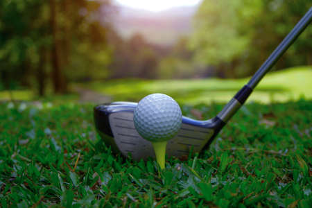 Golf ball on green grass ready to be struck on golf course background. Golf clubs and golf balls on a green lawn in a beautiful golf course with morning sunshine. Ready for golf in the first short.の写真素材