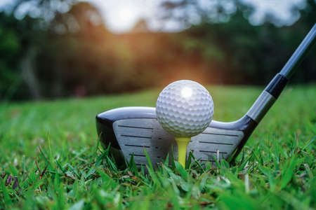 Golf ball on green grass ready to be struck on golf course background. Golf clubs and golf balls on a green lawn in a beautiful golf course with morning sunshine. Ready for golf in the first short.の写真素材