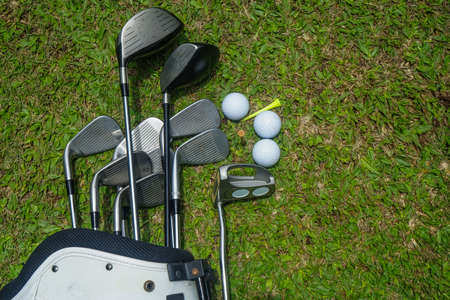 Closeup golf ball on tee ready to be shot. Golf ball on tee in the evening golf course with sunshine. Blurred set of golf clubs over green field background.の写真素材