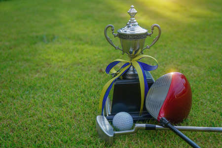 Golf champion trophy on green grass with golf clubs and golf ball in beautiful golf course. Sports that people around the world play during the holidays for health.の写真素材
