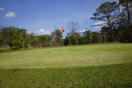 Landscape of a beautiful golf course at the sunset in the countryside. Red flag at the golf course in sunrise time.の写真素材