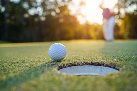Golfer practice training putting golf ball on the green, lens flare on sun set evening time.の写真素材