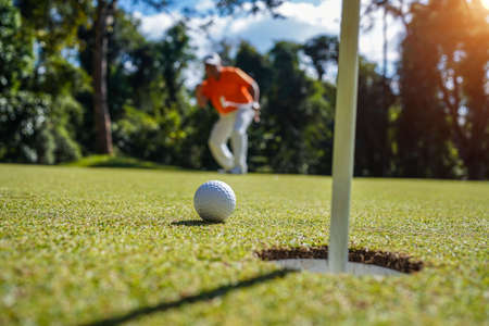 Hand hold golf ball with tee on course, golf course background. A golfer showing white golf ball in glove hand holding ,green grass nature blur background sunlight.の写真素材