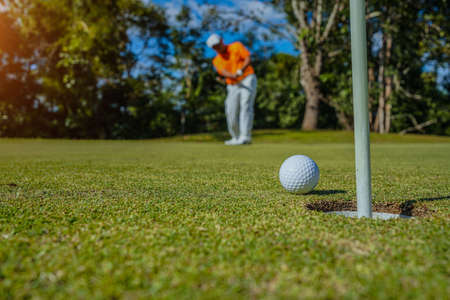 Golfer putting ball on the green golf, lens flare on sun set evening time. Golfer action to win after long putting golf ball in to the hole.の写真素材