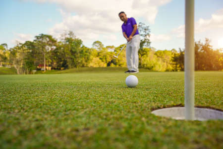 Golfer putting ball on the green golf, lens flare on sun set evening time. Golfer action to win after long putting golf ball in to the hole.の写真素材