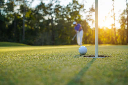 Golfer practice training putting golf ball on the green, lens flare on sun set evening time.の写真素材