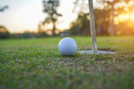 Golf clubs and ball on a green lawn in a beautiful golf course with morning sunshine. golf ball on green grass ready to hit on golf course background.の写真素材