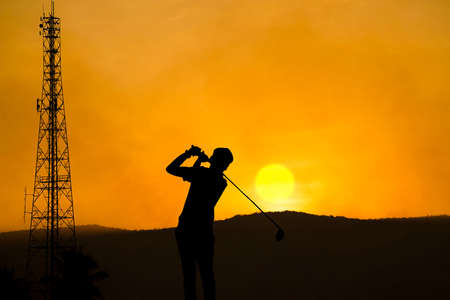 Golfers' hit golf ball toward the hole at sunset silhouetted. Golden morning sky in winter, misty high mountain background.の写真素材