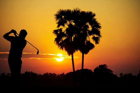 Golfers' hit golf ball toward the hole at sunset silhouetted. Golden morning sky in winter, misty high mountain background.の写真素材