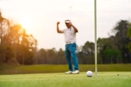 Golf balls that are going to be hole by golfers at the green grass golf course at sunset. Golfers are putting golf in the evening golf course, on sun set evening time.の写真素材