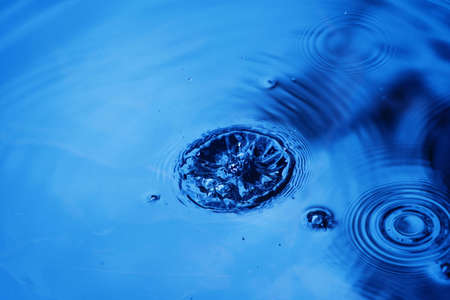 Raindrops falling on smooth surface of water. water droplets affect the surface, forming rings on the surface.の写真素材
